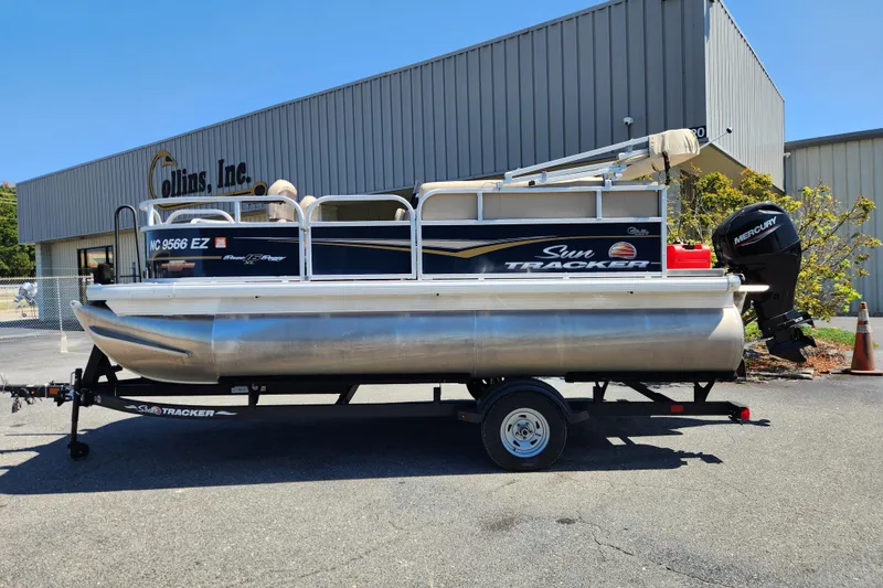 The Image of 2023 Sun Tracker Bass Buggy 16 XL Select pontoon boat on trailer, parked outside a building. - 0
