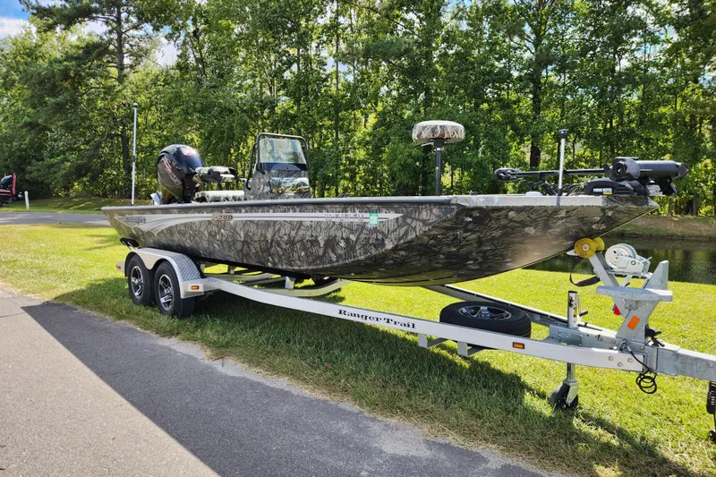 Slide: The Image of 2024 Ranger RB200 boat on trailer, parked on grass, surrounded by trees. - 1