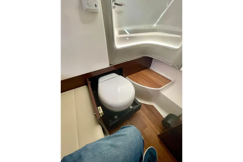 Slide: The Image of 2023 Chaparral 280 OSX boat interior with compact toilet and wooden flooring. - 33