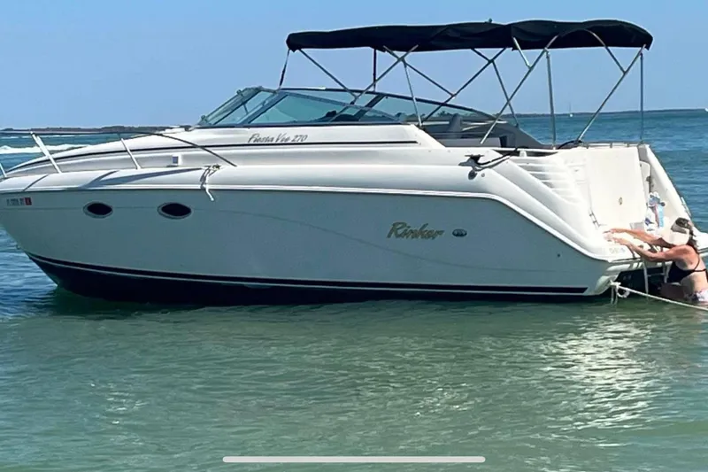 Slide: The Image of 2000 Rinker 270 Fiesta Vee boat anchored in calm waters with a person nearby. - 2