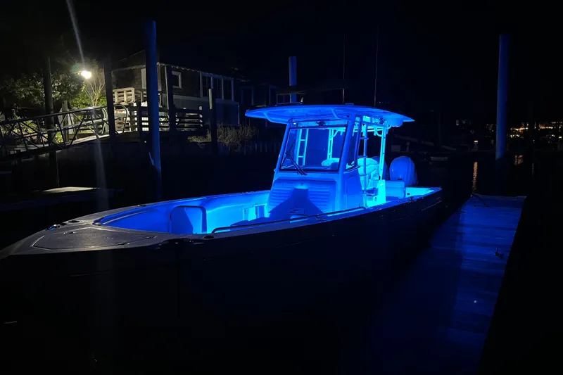 Slide: The Image of 2020 Edgewater 340CC boat illuminated with blue lights at night, docked in a marina. - 6