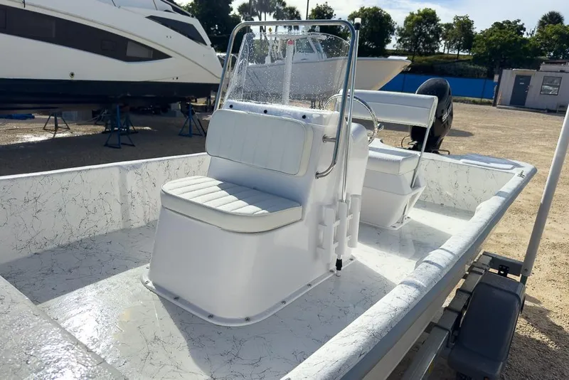 Slide: The Image of 2026 Coastal Skiff 171 boat with white seating and console, parked outdoors. - 11