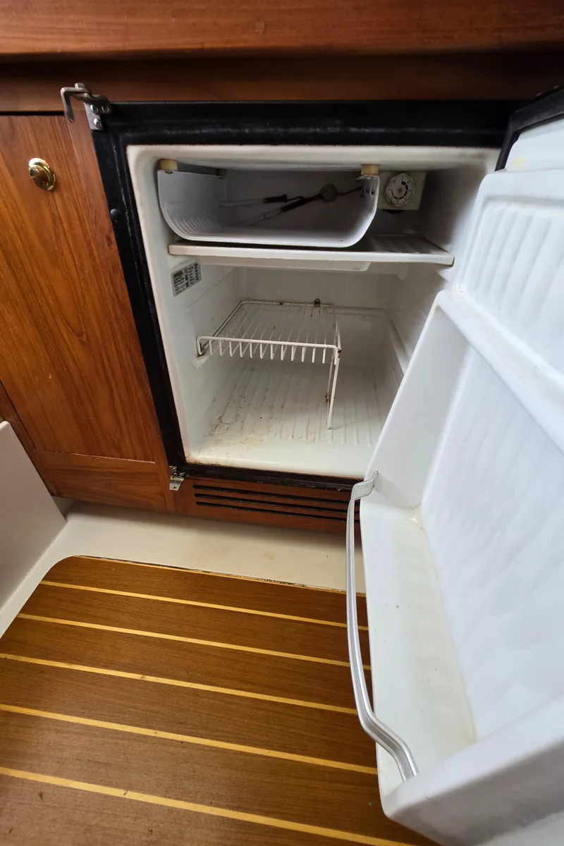 Slide: The Image of Open refrigerator inside 2001 Mainship Pilot 30 Sedan boat, featuring wooden cabinetry and flooring. - 42