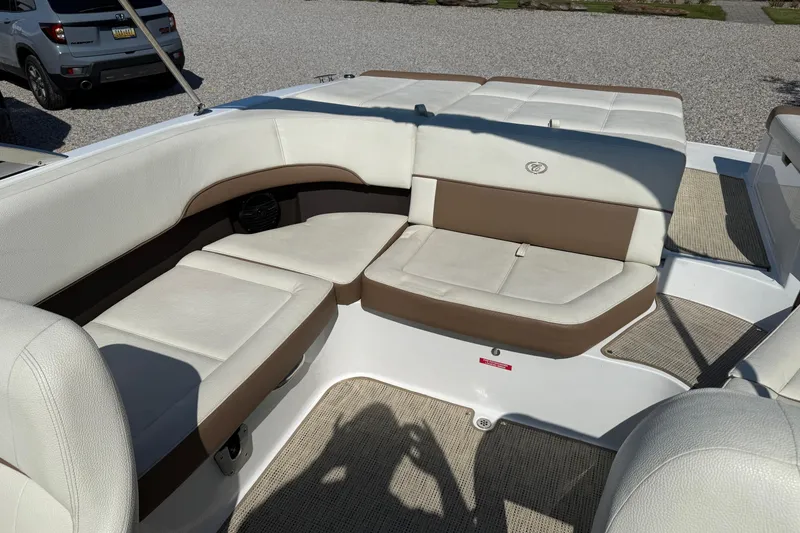 Slide: The Image of 2017 Cobalt 220S boat interior with beige and brown seating, parked on gravel. - 13