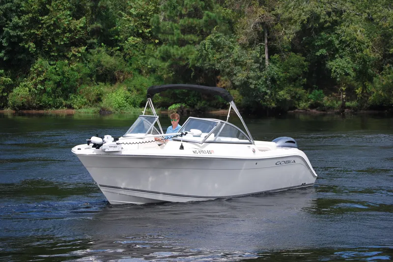 Slide: The Image of 2015 Cobia 220 Dual Console boat cruising on a calm river with lush green trees. - 3