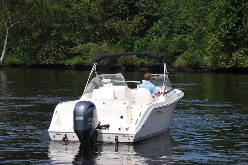 Slide: The Image of 2015 Cobia 220 Dual Console boat on a calm river, surrounded by lush greenery. - 4