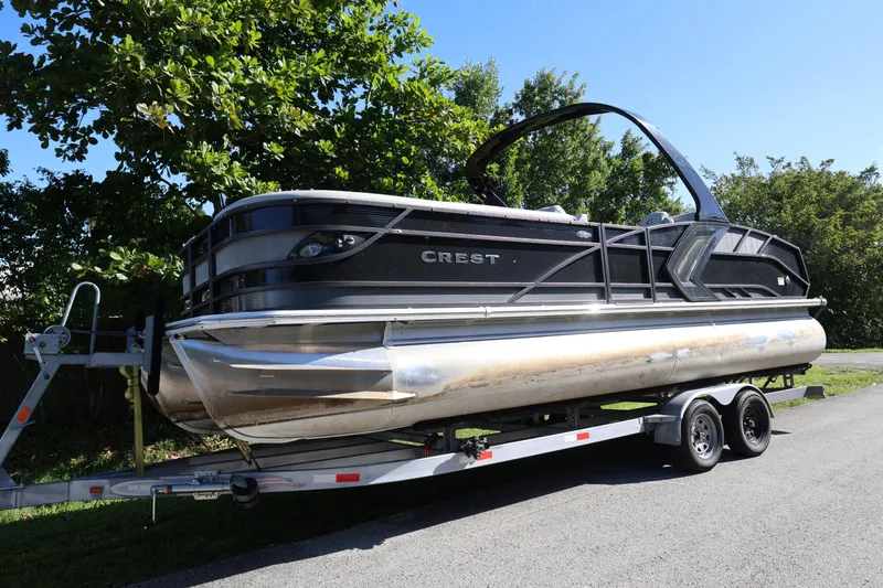 The Image of 2022 Crest Caribbean Platinum 250SLRC pontoon boat on trailer, surrounded by greenery. - 1