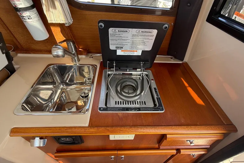 Slide: The Image of 2017 Ranger Tugs R-23 galley with sink and stove, featuring wood cabinetry. - 15
