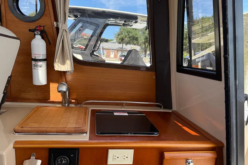 Slide: The Image of 2017 Ranger Tugs R-23 interior with kitchenette, fire extinguisher, and window view. - 17