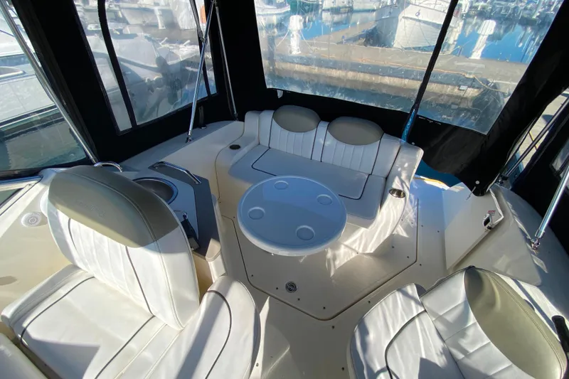 Slide: The Image of 2006 Sea Ray 240 Sundancer interior with white seating and round table, docked at marina. - 12