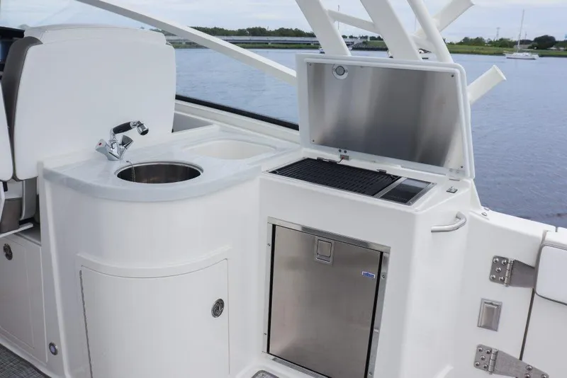 Slide: The Image of 2026 World Cat 325DC boat kitchenette with sink, grill, and storage by the water. - 24