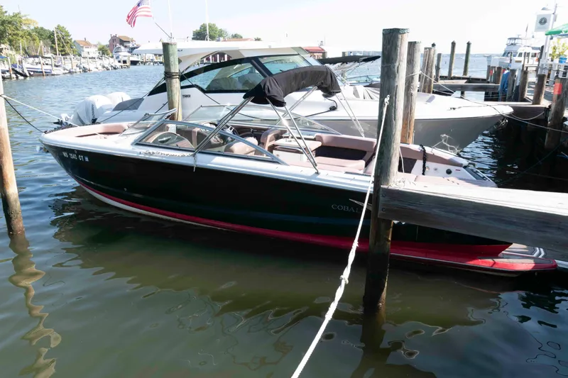 The Image of 2013 Cobalt A28 boat docked in a marina, surrounded by calm water and other vessels. - 0