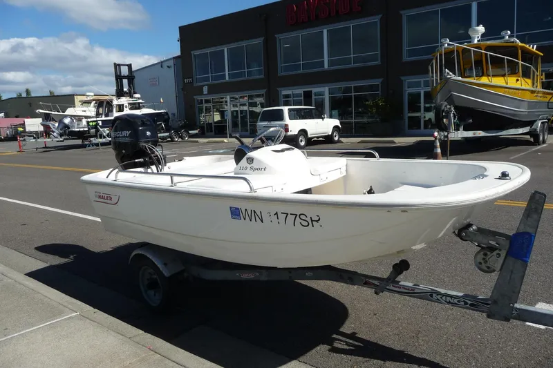 Slide: The Image of 2018 Boston Whaler 110 Sport boat on trailer, parked on street near dealership. - 2