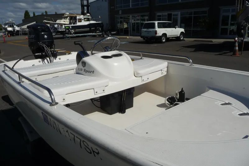 Slide: The Image of 2018 Boston Whaler 110 Sport boat with seating and outboard motor, parked outdoors. - 3