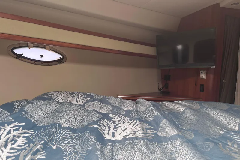 Slide: The Image of 2007 Cruisers Yachts 370 Express cabin with TV, porthole, and ocean-themed bedding. - 21