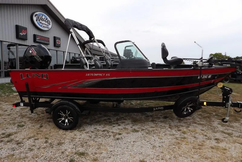 Slide: The Image of 2022 Lund 1875 Impact Sport boat in red and black, parked at a marine center. - 1