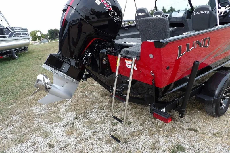 Slide: The Image of 2022 Lund 1875 Impact Sport boat with outboard motor and ladder, parked on gravel. - 44