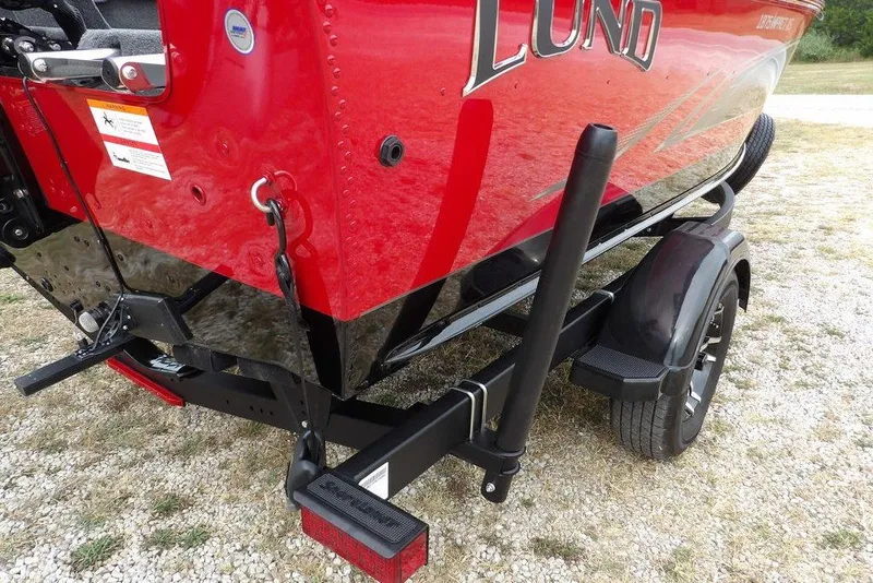 Slide: The Image of 2022 Lund 1875 Impact Sport boat on trailer, red and black design, parked on gravel. - 49
