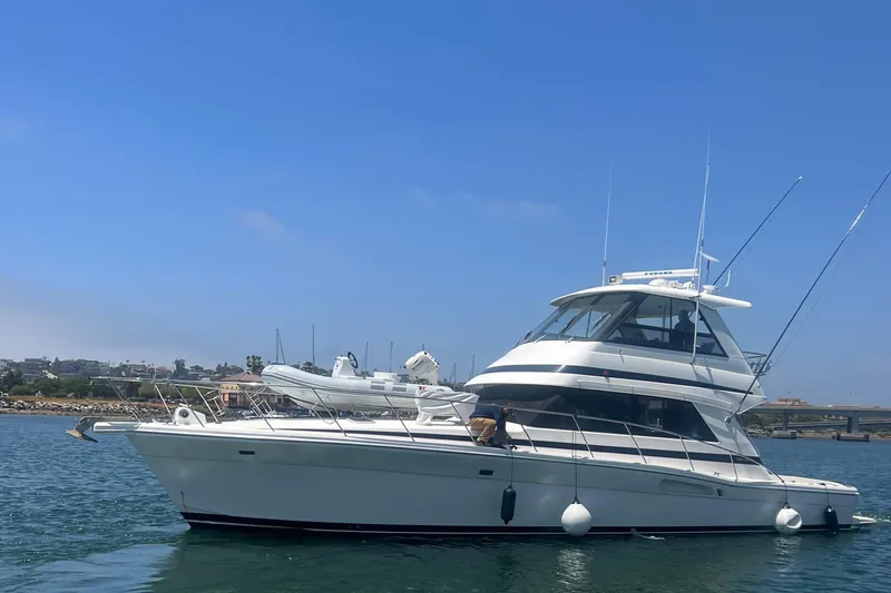 The Image of 2000 Riviera 48 Enclosed Flybridge yacht on calm water, clear sky background. - 0