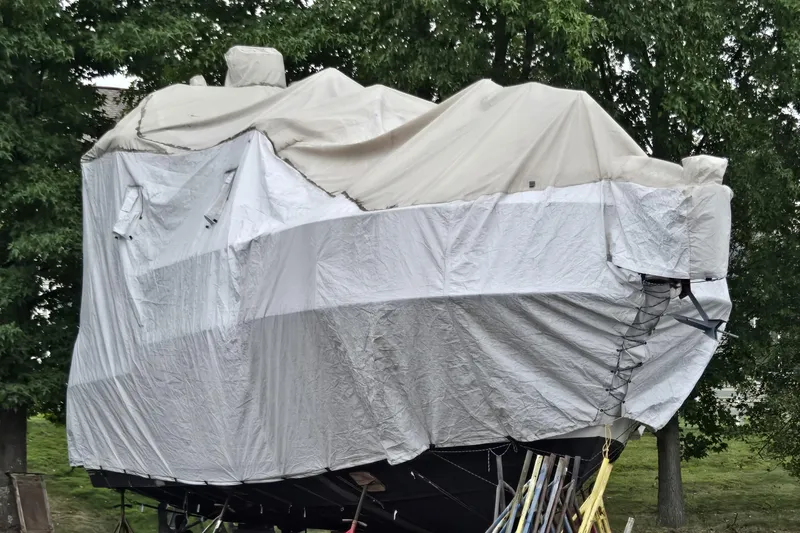 Slide: The Image of 1992 Carver 36 Aft Cabin boat covered with tarps, surrounded by trees. - 24