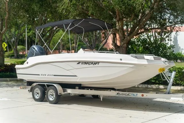 Slide: The Image of 2026 Starcraft SVX 211 OB boat on trailer, parked outdoors with trees in background. - 5