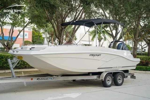 Slide: The Image of 2023 Starcraft SVX 231 OB DH boat on trailer, parked outdoors with trees in background. - 1