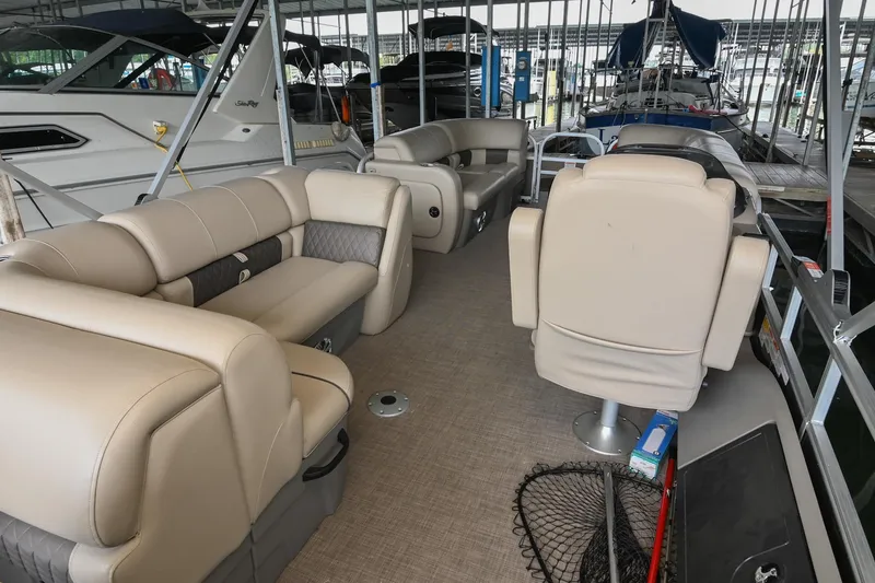 Slide: The Image of 2023 SUNTRACKER DLX 22 Sportfish pontoon boat interior with beige seating in marina. - 10