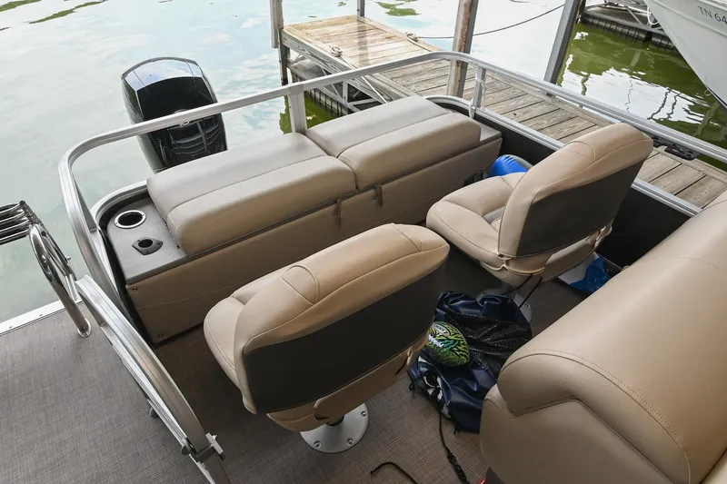 Slide: The Image of 2023 SUNTRACKER DLX 22 Sportfish boat interior with beige seating and motor, docked by water. - 8