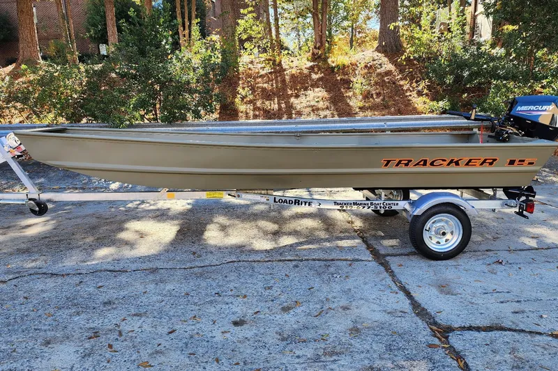 The Image of 2026 Tracker Grizzly 15 Jon boat on trailer, parked outdoors with trees in background. - 0