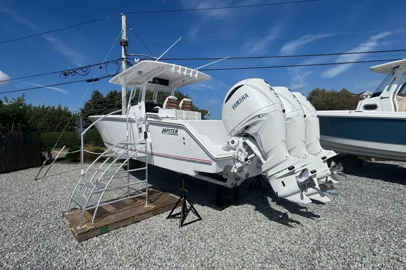 Slide: The Image of 2026 Jupiter 34 boat with Yamaha engines on gravel lot under blue sky. - 3
