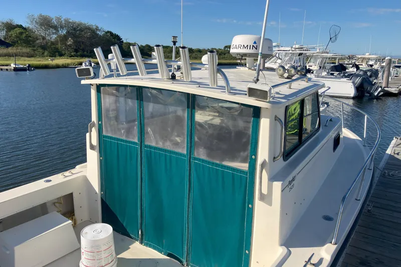 Slide: The Image of 2001 Parker 2520 Sport Cabin boat docked, featuring green cabin cover and fishing rod holders. - 5