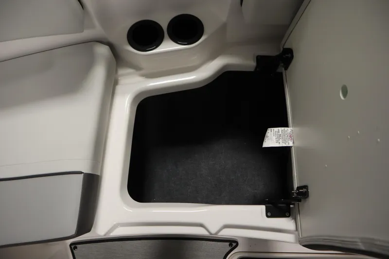 Slide: The Image of 2026 Yamaha Boats AR220 storage compartment with cup holders and open hatch. - 16