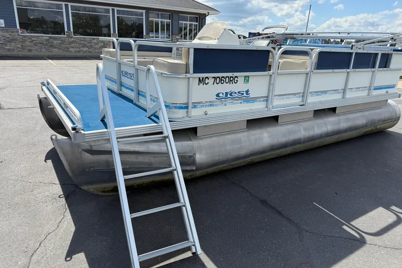 Slide: The Image of 1997 Crest 18 pontoon boat with ladder, parked on pavement under a partly cloudy sky. - 1