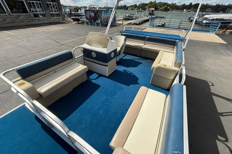 Slide: The Image of 1997 Crest 18 pontoon boat with blue and beige seating, docked by a lakeside marina. - 8
