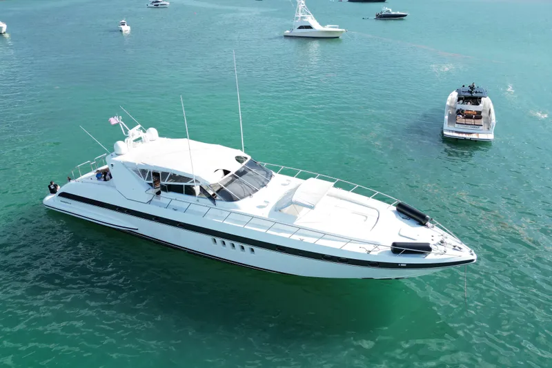 The Image of Luxurious 1999 Mangusta 80 yacht cruising in clear blue waters, surrounded by smaller boats. - 0