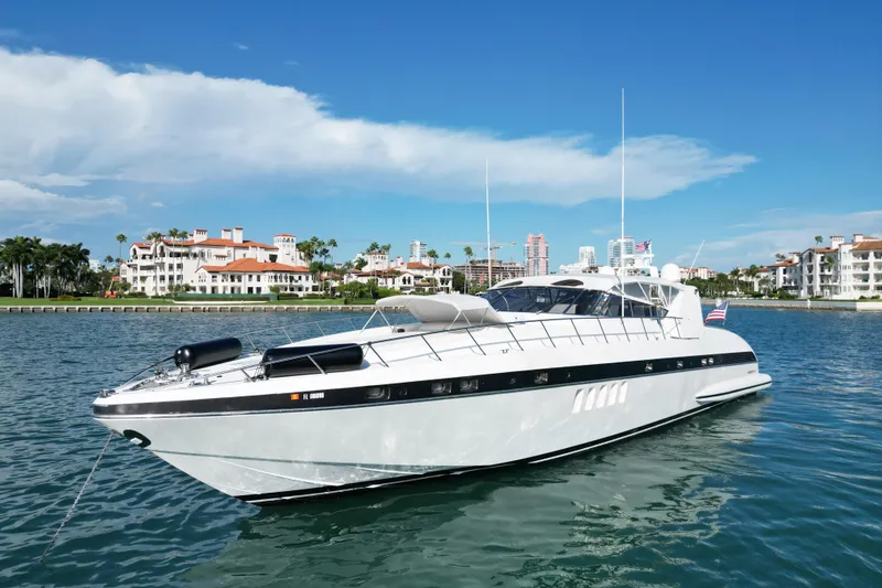 Slide: The Image of 1999 Mangusta 80 yacht cruising near luxury waterfront homes under a clear blue sky. - 3