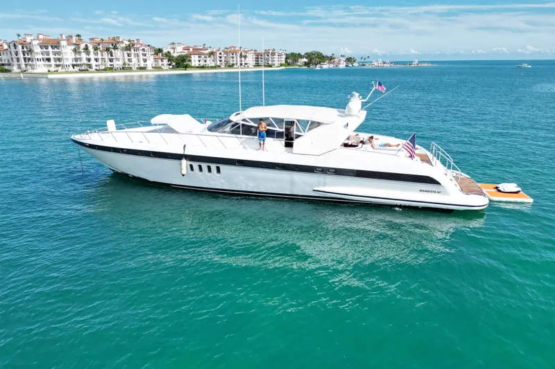 Slide: The Image of 1999 Mangusta 80 yacht cruising on turquoise waters near luxury waterfront residences. - 6