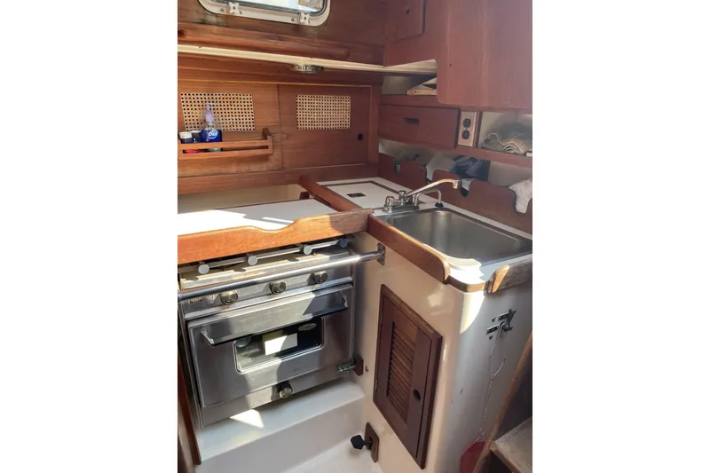 Slide: The Image of 1982 Tartan 33 yacht interior kitchen with stove, sink, and wooden cabinetry. - 2