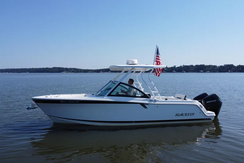 Slide: The Image of 2021 Blackfin 252 DC boat on calm lake with American flag, clear sky background. - 14