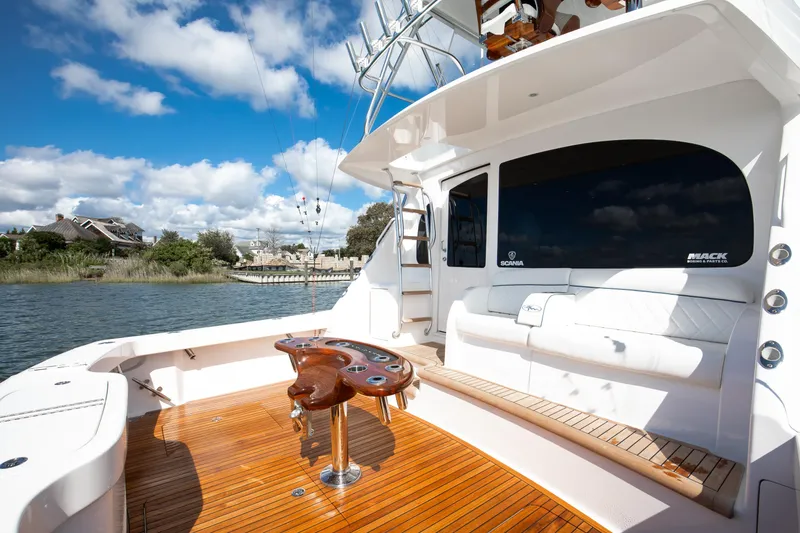 Slide: The Image of 2025 Viking 48 Convertible yacht deck with seating and fishing equipment, under a clear blue sky. - 38