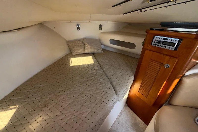 Slide: The Image of 2006 Pursuit 3370 Offshore cabin interior with bed, pillows, and wooden storage unit. - 18