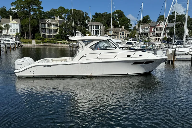 Slide: The Image of 2023 Pursuit OS 355 Offshore boat docked in a marina with waterfront homes. - 10