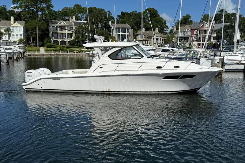 Slide: The Image of 2023 Pursuit OS 355 Offshore boat docked in a marina with waterfront homes. - 11