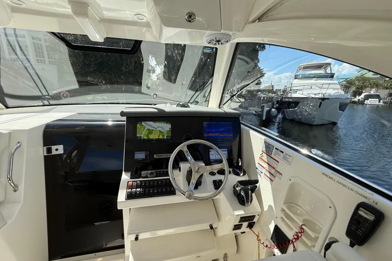 Slide: The Image of 2023 Pursuit OS 355 Offshore helm with navigation screens, docked near luxury yachts. - 26