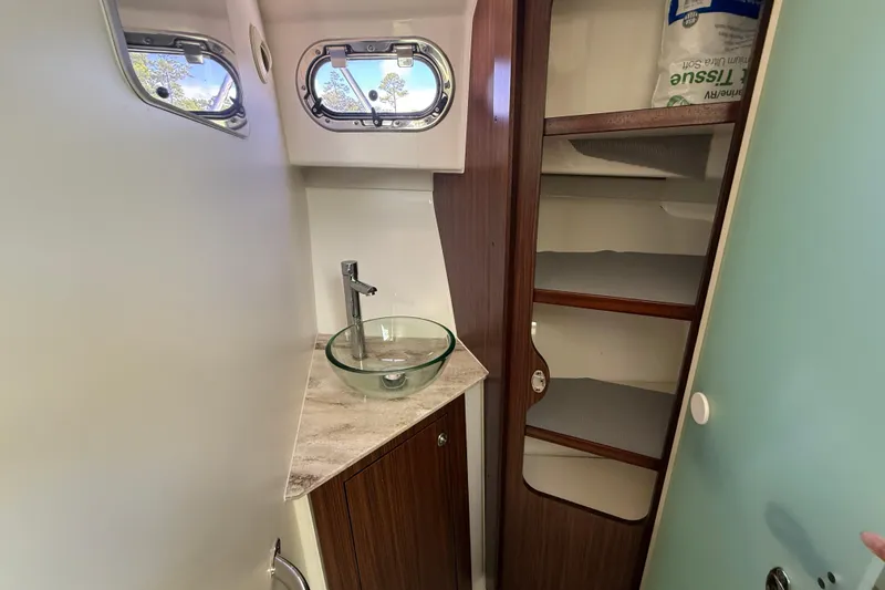 Slide: The Image of 2023 Pursuit OS 355 Offshore bathroom with glass sink, wooden cabinetry, and porthole windows. - 40
