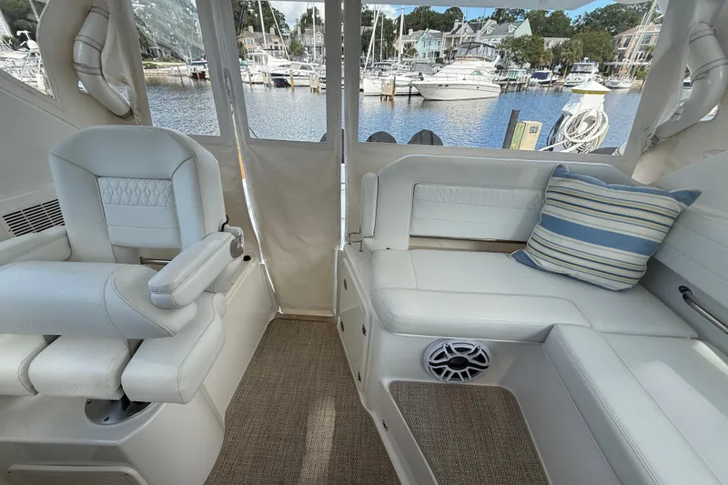 Slide: The Image of 2023 Pursuit OS 355 Offshore interior with white seating, striped pillow, and marina view. - 55