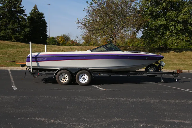The Image of 1996 Malibu Sunsetter LX boat on trailer in parking lot, surrounded by trees. - 0
