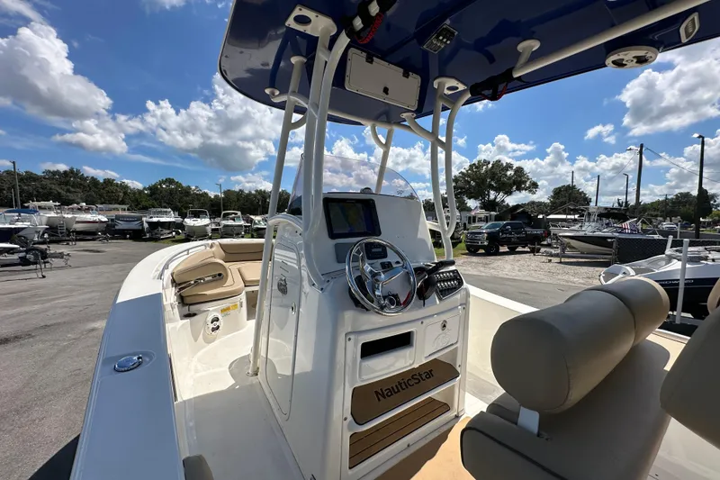 Slide: The Image of 2020 NauticStar 2302 Legacy boat interior with steering console and seating, under a blue sky. - 22