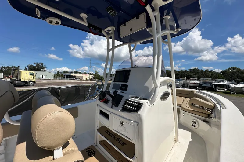 Slide: The Image of 2020 NauticStar 2302 Legacy boat interior with helm, seating, and clear blue sky. - 23