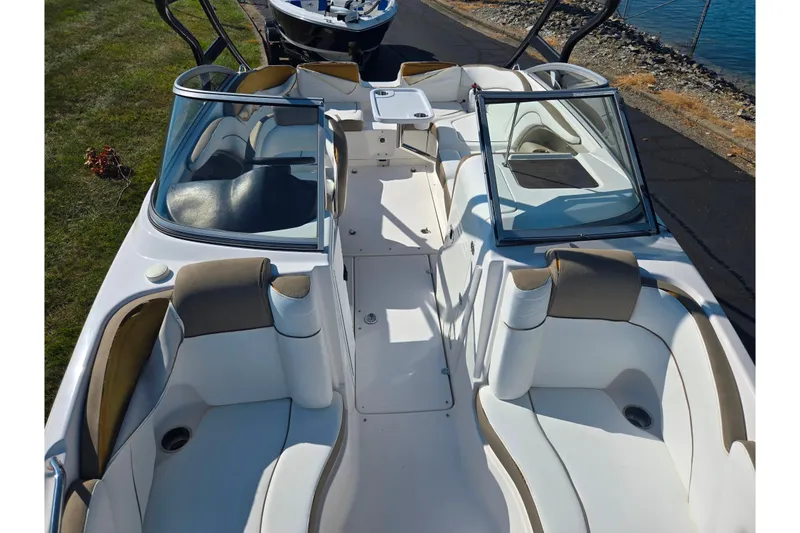 Slide: The Image of 2013 Yamaha Boats 242 Limited S interior with seating and windshield, docked by the water. - 21